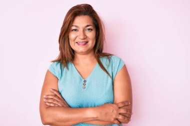 Orta yaşlı esmer, sıradan kıyafetler giyen mutlu yüzlü, kollarını kavuşturup kameraya bakan Latin bir kadın. pozitif kişi. 