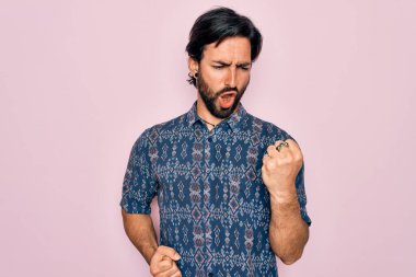 Pembe arka plan üzerine hippi tarzı giyinmiş genç, yakışıklı İspanyol bohem adam kolları havada ve gözleri kapalı bir şekilde başarıyı kutluyor ve şaşırıyor. Kazanan konsept.