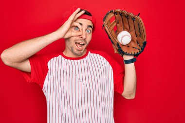 Genç yakışıklı, mavi gözlü, beyzbol oynayan, mutlu yüzlü, eldiven ve top kullanan, gülümseyen, el üstünde el işareti yapan, parmaklarının arasından bakan bir adam.