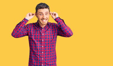 Ayılı yakışıklı genç adam rahat gömleğini giyiyor gülümsüyor kulakları parmaklarıyla çekiyor, komik bir jest. deneme sorunu 