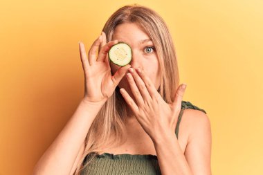 Genç, güzel, sarışın bir kadın, salatalık sümüğünü tutarak ağzını eliyle kapatmış, şok olmuş ve hata yapmaktan korkan. şaşırmış ifade 