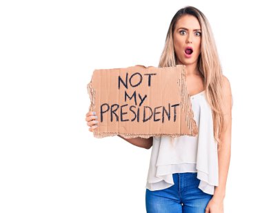 Genç, güzel, sarışın bir kadın, elinde karton pankartımı tutmuyor. Korkmuş ve şaşkına dönmüş bir şekilde ağzı açık, inançsız bir yüz. 