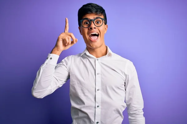孤立した紫色の背景にシャツと眼鏡を身に着けている若いハンサムなビジネスマンは 成功したアイデアで指を指しています 興奮し 第一番 — ストック写真