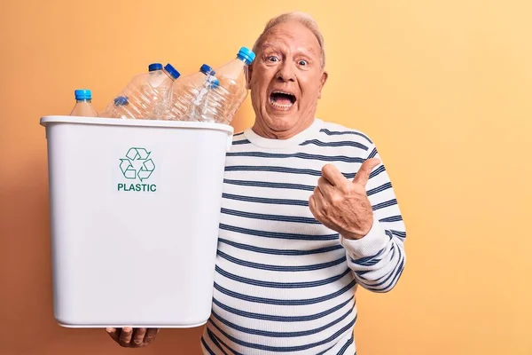 シニアハンサムな白髪男リサイクル保持Wazebasketフルのプラスチックボトルを指し親指上側に笑顔で幸せなオープン口 — ストック写真