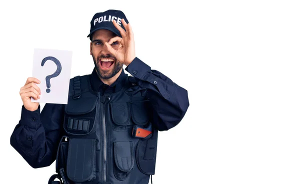 若いですハンサムな男とともに髭を身に着けて警察制服保持質問マーク笑顔幸せありますOk Signとともに手で目を通して指を見る — ストック写真