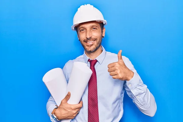 Jovem Homem Bonito Vestindo Arquiteto Hardhat Segurando Plantas Sorrindo Feliz — Fotografia de Stock