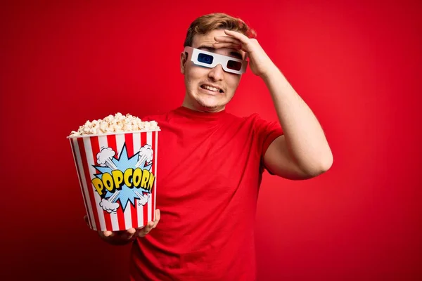 Młody Przystojny Rudzielec Oglądający Okulary Jedzący Popcorn Czerwonym Tle Zestresowany — Zdjęcie stockowe