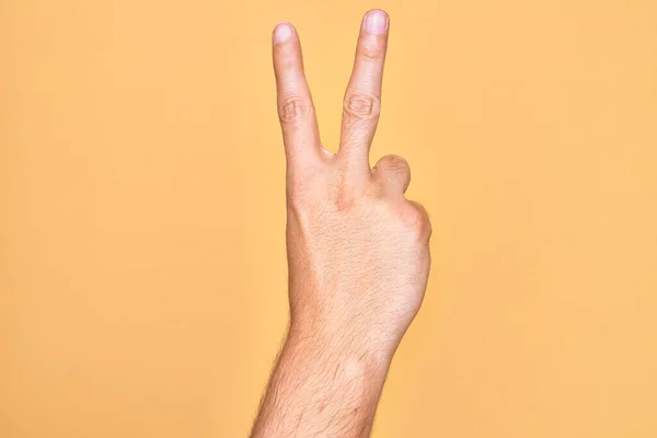 用手指在孤立的黄色背景上伸出援手的高加索年轻人数着2只手指 这预示着胜利和胜利的象征 — 图库照片