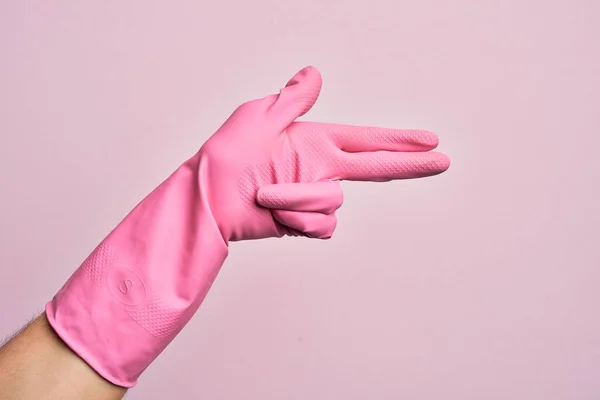 手握清洁手套的高加索年轻人用手指在孤立的粉色背景上摆弄火枪武器 瞄准射击符号 — 图库照片