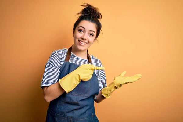Νεαρή Μελαχρινή Καθαρίστρια Γυναίκα Φορώντας Γάντια Καθαριότητας Πάνω Από Κίτρινο — Φωτογραφία Αρχείου