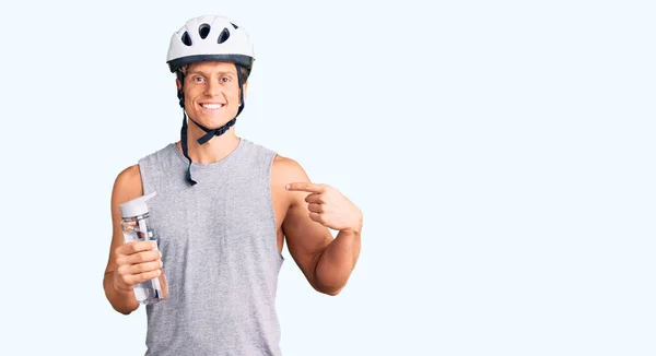 Jovem Homem Bonito Usando Capacete Bicicleta Segurando Garrafa Água Apontando — Fotografia de Stock