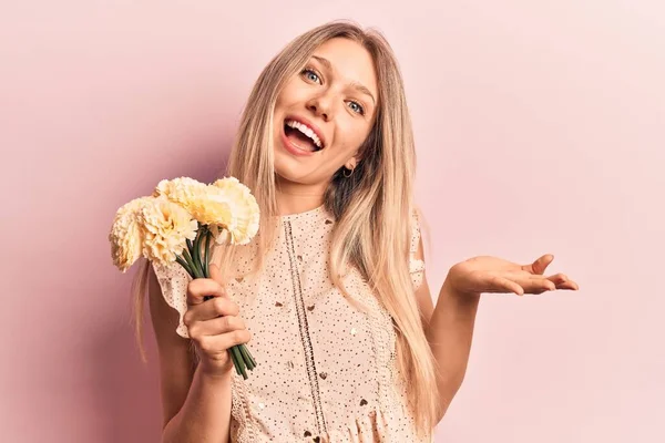 Jovem Loira Segurando Flores Celebrando Realização Com Sorriso Feliz Expressão — Fotografia de Stock