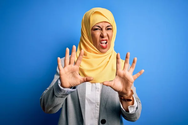 中年黑发女商人头戴穆斯林传统头巾 头戴蓝色背景的头巾 用手心 愤怒和沮丧的表情做着停下来的手势 — 图库照片