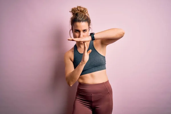 Young beautiful blonde sportswoman doing sport wearing sportswear over pink background Doing time out gesture with hands, frustrated and serious face
