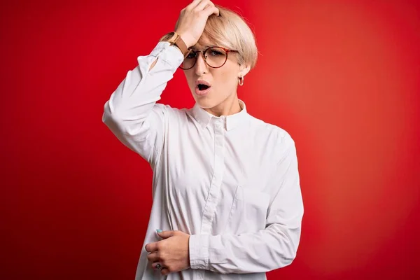 Młoda Blondynka Krótkimi Włosami Nosząca Okulary Czerwonym Tle Zaskoczona Pomyłką — Zdjęcie stockowe