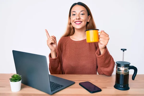 在办公室工作的年轻的黑发女人一边喝着一杯咖啡 一边高兴地把手和手指头指向旁边 — 图库照片