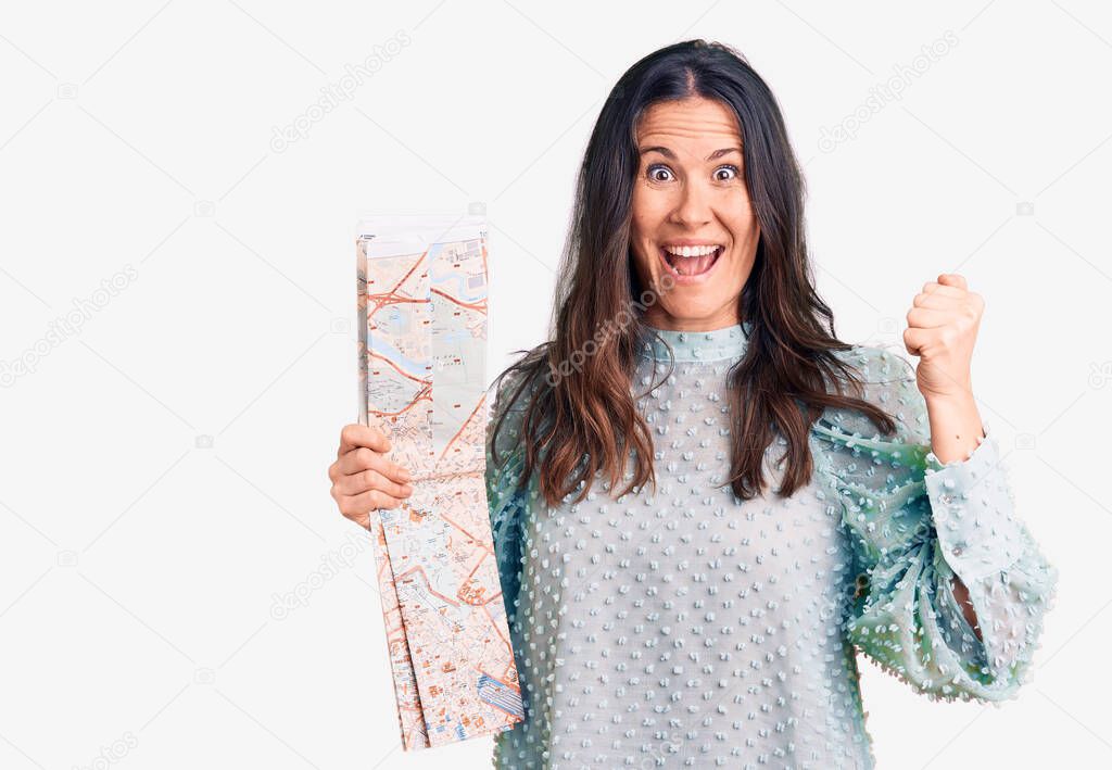 Young beautiful brunette woman holding city map screaming proud, celebrating victory and success very excited with raised arms 