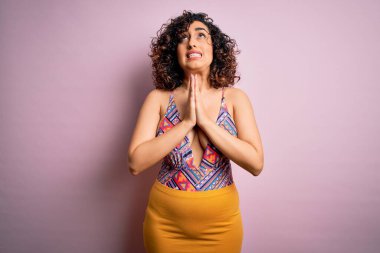 Genç, güzel bir Arap kadın, mayo ve pembe arka planda güneş gözlüğü takmış, yalvarıyor ve dua ediyor. Yüzünde umut ifadesi var. Çok duygusal ve endişeli. Yalvarıyorum..