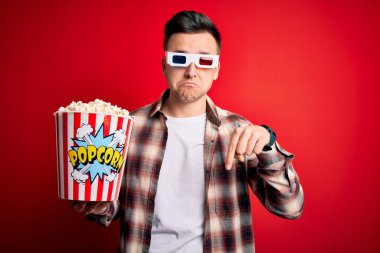 3 boyutlu film gözlüğü takan ve patlamış mısır yiyen, üzgün ve üzgün görünen, mutsuz ve depresif yönünü gösteren genç beyaz bir adam..