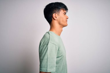 Genç ve yakışıklı bir adam günlük tişört giyiyor. İzole edilmiş beyaz arka plan üzerinde duruyor. Yan tarafa bakıyor, rahat profil pozu veriyor..