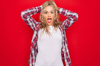 Genç, güzel, sarışın bir kadın yalnız kırmızı arka planda dikiliyor. Deli ve elleri başında, korkmuş ve ağzı açık bir şekilde şok geçirmekten korkuyor.