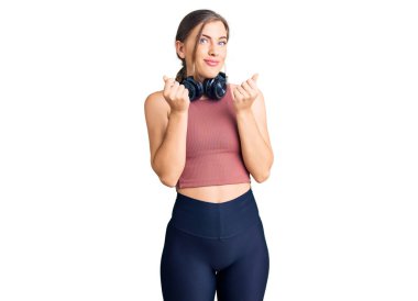 Güzel beyaz bir kadın spor kıyafetleri giyiyor ve kulaklık takıyor. Elleriyle para hareketi yapıyor. Maaş ödemesi istiyor. 