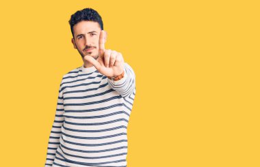 Latin asıllı genç bir adam, gündelik giysiler giyip parmağını kaldırmış ve kızgın bir ifade takınıyor. 