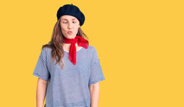 Fransız beresi ve çizgili tişört giyen genç, güzel sarışın kadın dudaklı balık suratı yapıyor, çılgınca ve komik bir jest. Komik ifade. 