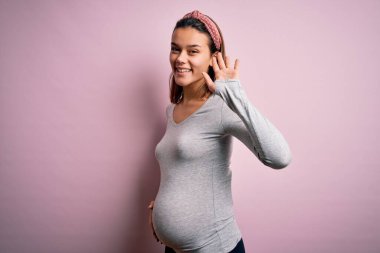 Genç, güzel, hamile bir kız pembe arka planda bebek bekliyor. Mutlu ve güler yüzlü bir şekilde selamlaşıyorlar.