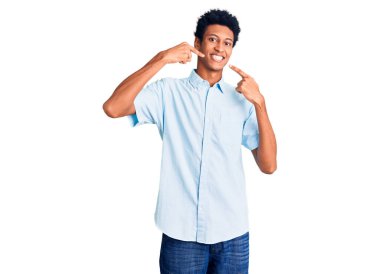 Gündelik kıyafetler giyen, neşeli gülümseyen, parmaklarıyla ve ağzıyla işaret eden Afrikalı genç bir Amerikalı. diş sağlığı kavramı. 