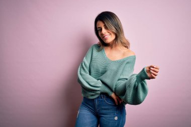 Moda kıyafetleri giyen genç ve güzel bir kadın. Manken, sokak tarzı giyiniyor. Pembe arka planda dikiliyor.