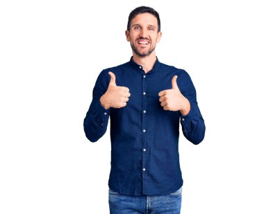 Genç ve yakışıklı bir adam, günlük tişört giyer, başarı işareti yapar, elleriyle olumlu jest yapar, gülümser ve mutlu olur. Neşeli ifade ve kazanan jest. 