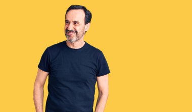 Orta yaşlı yakışıklı bir adam, sıradan tişörtler giyiyor. Yüzünde gülümseme, doğal bir ifade ile yan yana bakıyor. Kendinden emin gülen. 