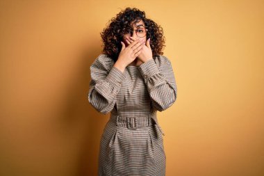 Sarı arka planda duran elbise ve gözlük takan güzel bir Arap iş kadını yanlışlıkla ağızlarını kapatarak şok geçirdi. Gizli konsept.