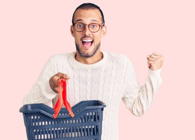 Süpermarket alışveriş sepetini tutan yakışıklı genç adam gururla bağırıyor, zaferi ve başarıyı kutluyor. Kollarını kaldırıp heyecanla bekliyor. 