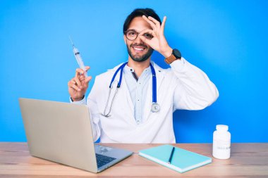 Klinikteki yakışıklı İspanyol doktor elinde şırıngayla gülümsüyor. Mutluluktan gülümsüyor. 