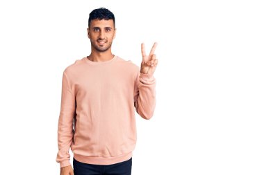 Gündelik kıyafetler giyen genç İspanyol adam kameraya bakıp zafer işareti yaparken parmaklarını gösteriyor. İki numara.. 