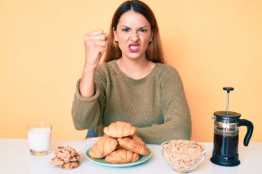 Genç esmer kadın masada oturmuş kahvaltısını yapıyor öfkeyle bağırıyor, öfkeyle bağırıyor ve el kaldırıyor. 