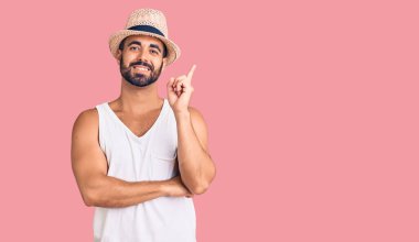 Gündelik yaz şapkası takan, yüzünde kocaman bir gülümseme olan, eli ve parmağı kameraya bakan genç İspanyol bir adam.. 