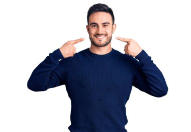 Gündelik kıyafetler giyen, neşeli gülümseyen, parmaklarıyla ve ağzıyla işaret eden genç yakışıklı bir adam. diş sağlığı kavramı. 