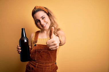 Sarışın, güzel bir kadın izole edilmiş sarı arka planda bira içiyor. Kocaman gülümsüyor. Tamam işareti yapıyor.