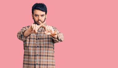 Gündelik kıyafetler giyen genç İspanyol adam reddedilme ifadesini negatif işaret yaparak parmaklarını çapraz yapıyor. 