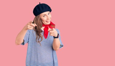 Fransız bereli ve çizgili tişörtlü genç, güzel sarışın kadın kamerayı mutlu ve komik yüzüyle işaret ediyor. iyi enerji ve titreşimler. 