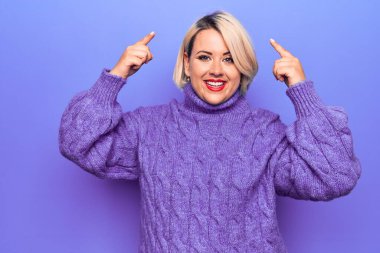 Güzel sarışın, iri yarı, balıkçı yaka kazak giyen, mor arka planda gülümseyen, iki eliyle kafasını gösteren güzel bir kadın. Harika fikir ya da düşünce, iyi hafıza.