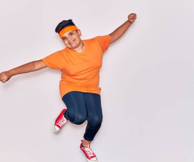 Spor kıyafetleri giyen sevimli İspanyol çocuk mutlu gülümsüyor. İzole edilmiş beyaz arka planda yüzünde gülümsemeyle zıpla