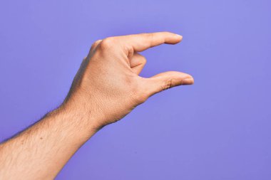 İzole edilmiş mor arka plan üzerinde parmaklarını gösteren beyaz bir adamın eli. Görünmez bir şeyi alıyor, parmakları boşluğu gösteren bir nesneyi tutuyor.