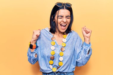 Gündelik giysiler giyen genç, güzel Latin bir kadın. Başarının şaşkınlığını ve şaşkınlığını kolları havada, gözleri kapalı kutluyor. 