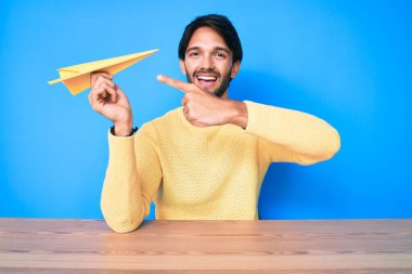 Kağıt uçak tutan yakışıklı İspanyol adam mutlu bir şekilde elini ve parmağını gösterdi. 