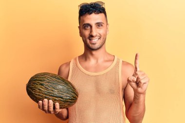 Elinde kavun tutan genç İspanyol bir adam bir fikirle gülümsüyor ya da bir soru işareti yapıyor mutlu bir yüzle, bir numara 