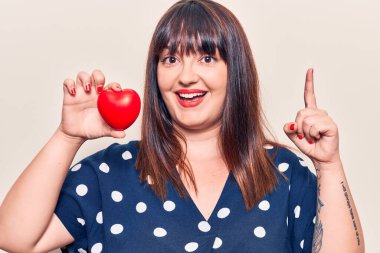 Kalbi tutan genç ve iri bir kadın bir fikir ya da soruyla şaşkın bir şekilde mutlu bir yüzle işaret ediyor. 